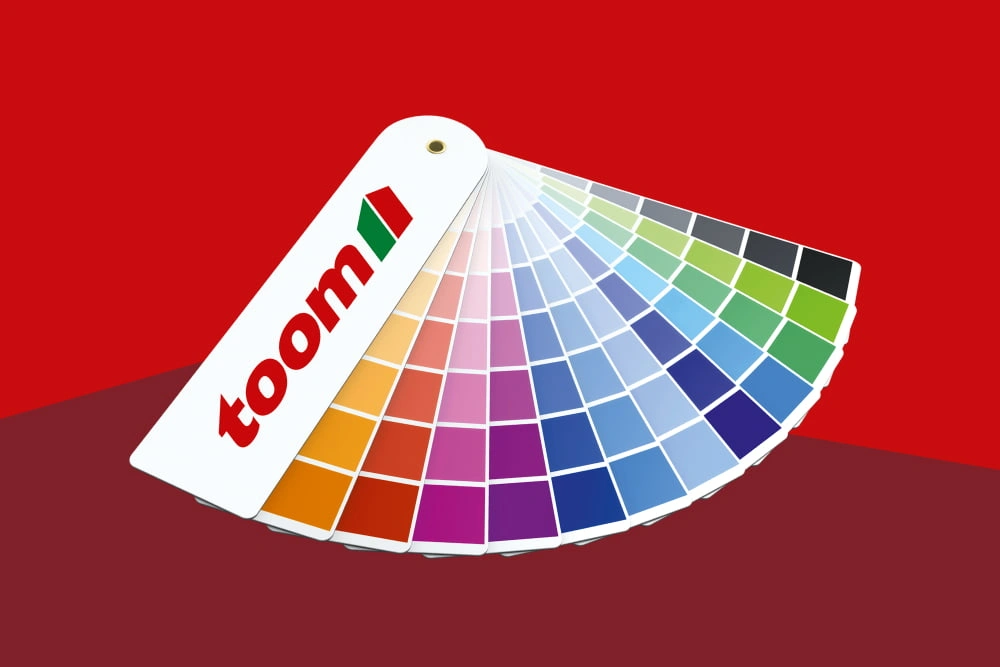 Ein aufgefächerter Farbfächer mit vielen bunten Farbtönen vor einem roten Hintergrund.